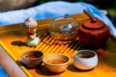 Tahta tepside masada çaylı çaydanlık, çaydanlık, bardak. Adam, eller çay döküyor.