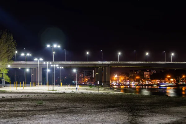 Lekplats på sandstranden. Bron över floden och natt staden på bakgrunden. — Stockfoto