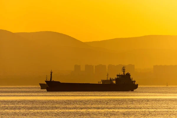 Golden sunset, silhouette of the city and cargo ship. Beautiful architecort by the sea on the background of the sunset — Stock Photo, Image