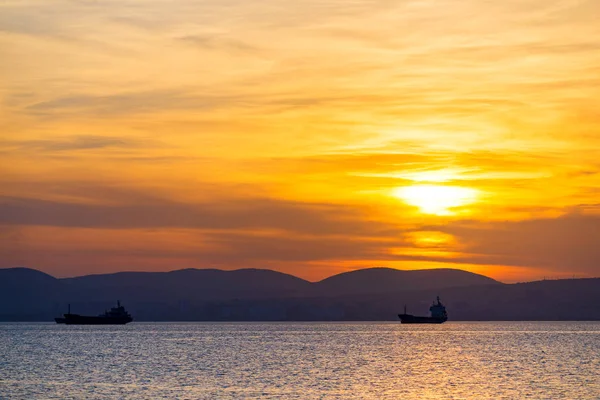 Tramonto dorato, silhouette della città e nave da carico. Bellissima architettura sul mare sullo sfondo del tramonto — Foto Stock