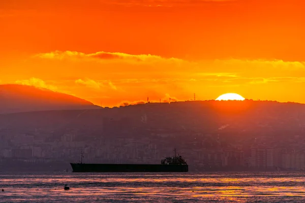 Vacker solnedgång bland molnen. Solstrålarna är helt enkelt vackra. Stad, berg och fartyg i havet — Stockfoto