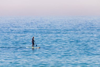 Dalgıç kıyafetli kürekçi ayağa kalkıp denizde kürek çekiyor. Asgari görüntü