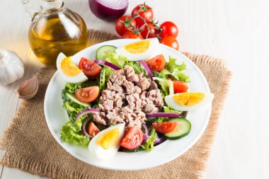 Domates, roka, ton balığı, yumurta, roka, kraker ve baharattan yapılmış taze balık salatası. Tahta arka planda beyaz bir kasede Sezar salatası.