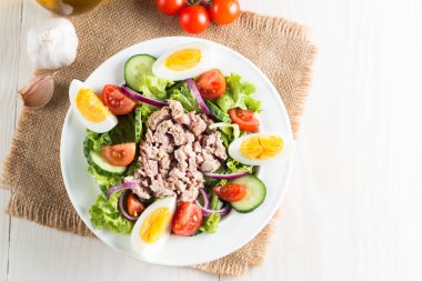 Domates, roka, ton balığı, yumurta, roka, kraker ve baharattan yapılmış taze balık salatası. Tahta arka planda beyaz bir kasede Sezar salatası.