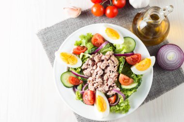 Domates, roka, ton balığı, yumurta, roka, kraker ve baharattan yapılmış taze balık salatası. Tahta arka planda beyaz bir kasede Sezar salatası.