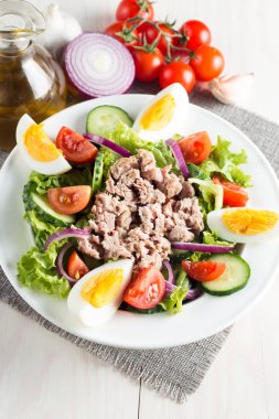 Domates, roka, ton balığı, yumurta, roka, kraker ve baharattan yapılmış taze balık salatası. Tahta arka planda beyaz bir kasede Sezar salatası.