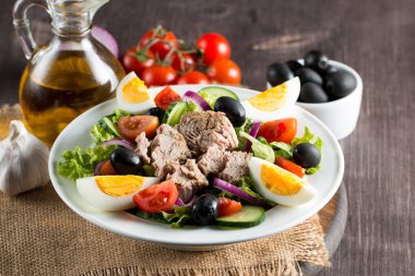 Domates, roka, ton balığı, yumurta, roka, kraker ve baharattan yapılmış taze balık salatası. Tahta arka planda beyaz bir kasede Sezar salatası.