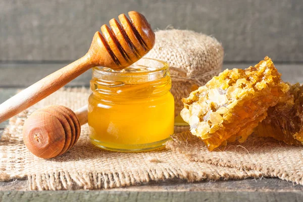 Tatlım gelen ahşap bal ayı gri rustik ahşap arka plan üzerinde bir kavanoza damlama