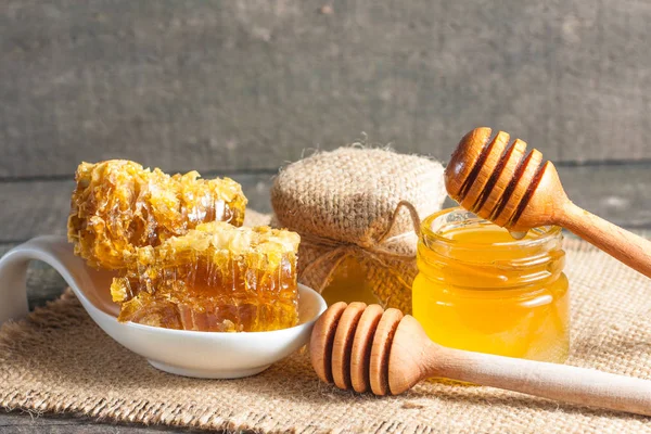 Tatlım gelen ahşap bal ayı gri rustik ahşap arka plan üzerinde bir kavanoza damlama