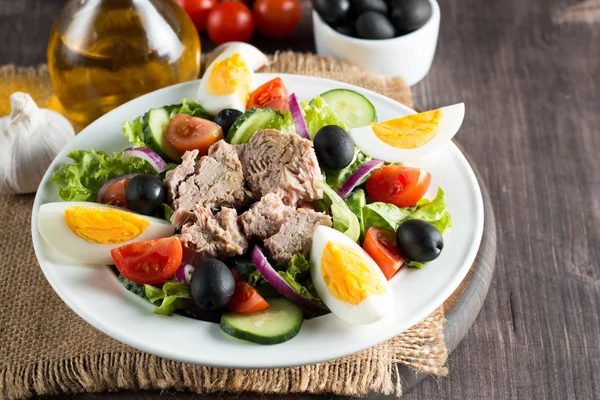 Domates, roka, ton balığı, yumurta, roka, kraker ve baharattan yapılmış taze balık salatası. Tahta arka planda beyaz bir kasede Sezar salatası.