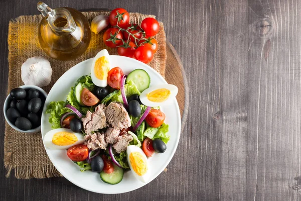 Domates, roka, ton balığı, yumurta, roka, kraker ve baharattan yapılmış taze balık salatası. Tahta arka planda beyaz bir kasede Sezar salatası.