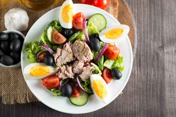 Domates, roka, ton balığı, yumurta, roka, kraker ve baharattan yapılmış taze balık salatası. Tahta arka planda beyaz bir kasede Sezar salatası.