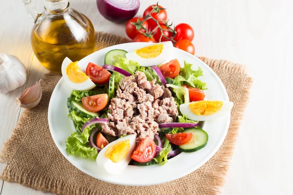 Domates, roka, ton balığı, yumurta, roka, kraker ve baharattan yapılmış taze balık salatası. Tahta arka planda beyaz bir kasede Sezar salatası.