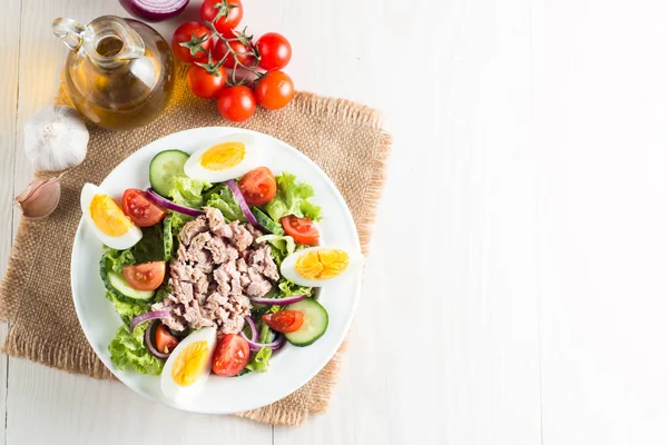 Domates, roka, ton balığı, yumurta, roka, kraker ve baharattan yapılmış taze balık salatası. Tahta arka planda beyaz bir kasede Sezar salatası.