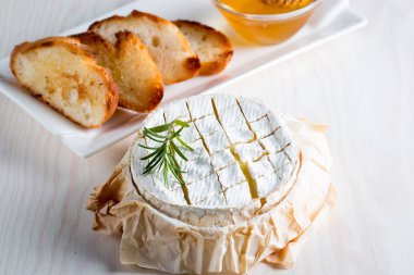 Pişmiş camembert peyniri. Taze Brie peyniri ve bir dilim fındık, tatlım, biberiye ile ahşap bir gemide, baget ekmek ızgara tost ve yaprakları. Peynir Brie türü. İtalyan, Fransız peynir.