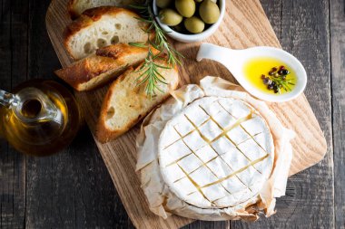 Pişmiş camembert peyniri. Taze Brie peyniri ve bir dilim fındık, tatlım, biberiye ile ahşap bir gemide, baget ekmek ızgara tost ve yaprakları. Peynir Brie türü. İtalyan, Fransız peynir.