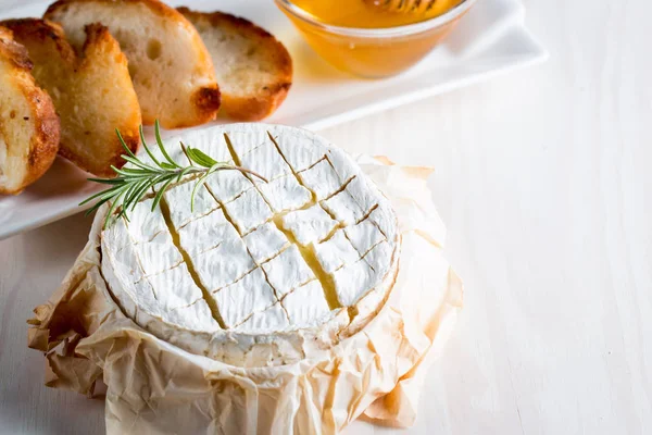 Pişmiş camembert peyniri. Taze Brie peyniri ve bir dilim fındık, tatlım, biberiye ile ahşap bir gemide, baget ekmek ızgara tost ve yaprakları. Peynir Brie türü. İtalyan, Fransız peynir.