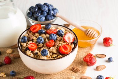 Sağlıklı kahvaltı konsepti ile yulaf gevreği ve rustik arka plan üzerinde taze çilek. Granola yapılan yemekleri müsli. Böğürtlen, muslie, çilek, yaban mersini ve bal ile sağlıklı muz smoothie.