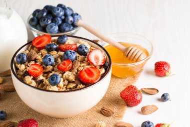 Sağlıklı kahvaltı konsepti ile yulaf gevreği ve rustik arka plan üzerinde taze çilek. Granola yapılan yemekleri müsli. Böğürtlen, muslie, çilek, yaban mersini ve bal ile sağlıklı muz smoothie.