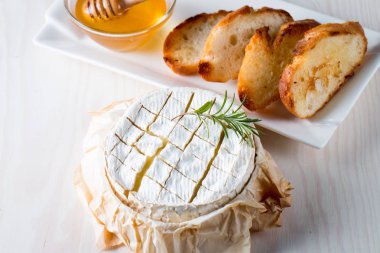 Pişmiş camembert peyniri. Taze Brie peyniri ve bir dilim fındık, tatlım, biberiye ile ahşap bir gemide, baget ekmek ızgara tost ve yaprakları. Peynir Brie türü. İtalyan, Fransız peynir.