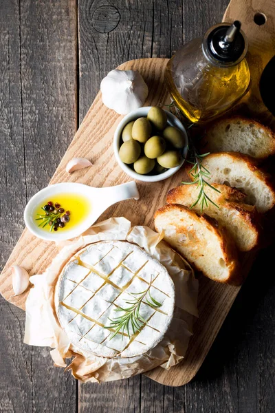 Baked camembert cheese. Fresh Brie cheese and a slice on a wooden board with nuts, honey, rosemary, baguette bread grilled toasts and leaves. Brie type of cheese. Italian, French cheese.