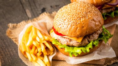 Ev yapımı Hamburger bira ile yakın çekim fotoğraf sığır eti, soğan, domates, marul, peynir ve baharat yaptı. Taze hamburger tatlı patates kızartması ve cips ile ahşap rustik tabloda.