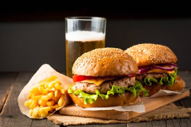 Ev yapımı Hamburger bira ile yakın çekim fotoğraf sığır eti, soğan, domates, marul, peynir ve baharat yaptı. Taze hamburger tatlı patates kızartması ve cips ile ahşap rustik tabloda.