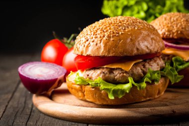 Ev yapımı Hamburger bira ile yakın çekim fotoğraf sığır eti, soğan, domates, marul, peynir ve baharat yaptı. Taze hamburger tatlı patates kızartması ve cips ile ahşap rustik tabloda.