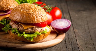 Ev yapımı Hamburger bira ile yakın çekim fotoğraf sığır eti, soğan, domates, marul, peynir ve baharat yaptı. Taze hamburger tatlı patates kızartması ve cips ile ahşap rustik tabloda.