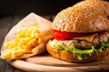 Ev yapımı Hamburger bira ile yakın çekim fotoğraf sığır eti, soğan, domates, marul, peynir ve baharat yaptı. Taze hamburger tatlı patates kızartması ve cips ile ahşap rustik tabloda.