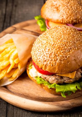 Ev yapımı Hamburger bira ile yakın çekim fotoğraf sığır eti, soğan, domates, marul, peynir ve baharat yaptı. Taze hamburger tatlı patates kızartması ve cips ile ahşap rustik tabloda.