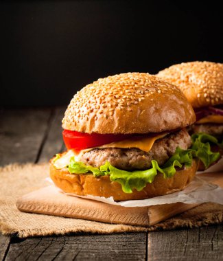 Ev yapımı Hamburger bira ile yakın çekim fotoğraf sığır eti, soğan, domates, marul, peynir ve baharat yaptı. Taze hamburger tatlı patates kızartması ve cips ile ahşap rustik tabloda.