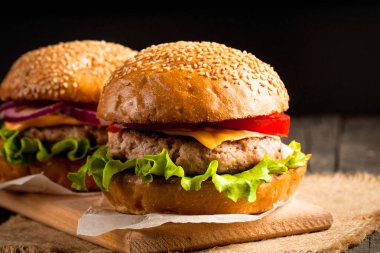 Ev yapımı Hamburger bira ile yakın çekim fotoğraf sığır eti, soğan, domates, marul, peynir ve baharat yaptı. Taze hamburger tatlı patates kızartması ve cips ile ahşap rustik tabloda.