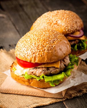 Ev yapımı Hamburger bira ile yakın çekim fotoğraf sığır eti, soğan, domates, marul, peynir ve baharat yaptı. Taze hamburger tatlı patates kızartması ve cips ile ahşap rustik tabloda.