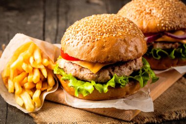 Ev yapımı Hamburger bira ile yakın çekim fotoğraf sığır eti, soğan, domates, marul, peynir ve baharat yaptı. Taze hamburger tatlı patates kızartması ve cips ile ahşap rustik tabloda.