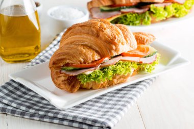 Taze kruvasan veya sandviç salata, jambon, jamon, jambon, salam, peynir, tavuk, domates ahşap arka plan ile. Sabah kahvaltı kavramı. Sağlıklı ve fast food.