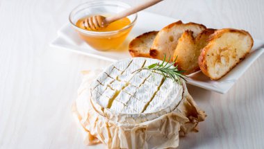Pişmiş camembert peyniri. Taze Brie peyniri ve bir dilim fındık, tatlım, biberiye ile ahşap bir gemide, baget ekmek ızgara tost ve yaprakları. Peynir Brie türü. İtalyan, Fransız peynir.