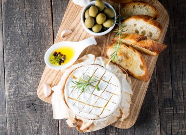 Pişmiş camembert peyniri. Taze Brie peyniri ve bir dilim fındık, tatlım, biberiye ile ahşap bir gemide, baget ekmek ızgara tost ve yaprakları. Peynir Brie türü. İtalyan, Fransız peynir.