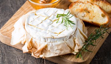 Pişmiş camembert peyniri. Taze Brie peyniri ve bir dilim fındık, tatlım, biberiye ile ahşap bir gemide, baget ekmek ızgara tost ve yaprakları. Peynir Brie türü. İtalyan, Fransız peynir.