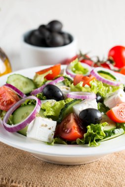 Kiraz domates, ruccola, roka, beyaz peynir, zeytin, salatalık, soğan ve baharat taze Yunan salatası yaptı. Sezar salatası ahşap arka plan üzerinde beyaz bir kase. Sağlıklı organik beslenme gıda kavramı.