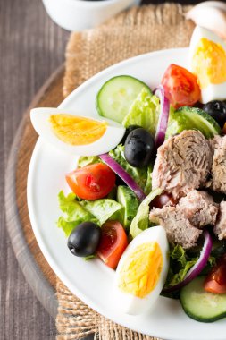 Kiraz domates, ruccola, roka, beyaz peynir, zeytin, salatalık, soğan ve baharat taze Yunan salatası yaptı. Sezar salatası ahşap arka plan üzerinde beyaz bir kase. Sağlıklı organik beslenme gıda kavramı.