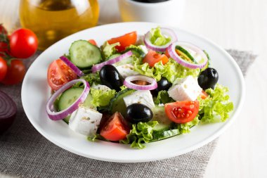 Kiraz domates, ruccola, roka, beyaz peynir, zeytin, salatalık, soğan ve baharat taze Yunan salatası yaptı. Sezar salatası ahşap arka plan üzerinde beyaz bir kase. Sağlıklı organik beslenme gıda kavramı.