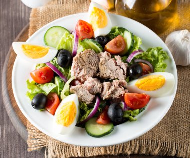 Domates, roka, ton balığı, yumurta, roka, kraker ve baharattan yapılmış taze balık salatası. Tahta arka planda beyaz bir kasede Sezar salatası.