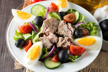 Domates, roka, ton balığı, yumurta, roka, kraker ve baharattan yapılmış taze balık salatası. Tahta arka planda beyaz bir kasede Sezar salatası.