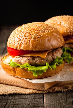 Ev yapımı Hamburger bira ile yakın çekim fotoğraf sığır eti, soğan, domates, marul, peynir ve baharat yaptı. Taze hamburger tatlı patates kızartması ve cips ile ahşap rustik tabloda.