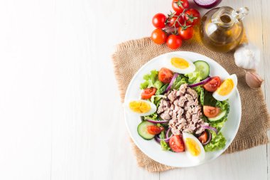 Domates, roka, ton balığı, yumurta, roka, kraker ve baharattan yapılmış taze balık salatası. Tahta arka planda beyaz bir kasede Sezar salatası.