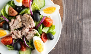 Domates, roka, ton balığı, yumurta, roka, kraker ve baharattan yapılmış taze balık salatası. Tahta arka planda beyaz bir kasede Sezar salatası.