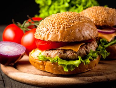Ev yapımı Hamburger bira ile yakın çekim fotoğraf sığır eti, soğan, domates, marul, peynir ve baharat yaptı. Taze hamburger tatlı patates kızartması ve cips ile ahşap rustik tabloda.