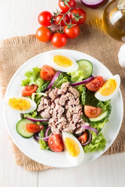 Domates, roka, ton balığı, yumurta, roka, kraker ve baharattan yapılmış taze balık salatası. Tahta arka planda beyaz bir kasede Sezar salatası.