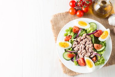 Domates, roka, ton balığı, yumurta, roka, kraker ve baharattan yapılmış taze balık salatası. Tahta arka planda beyaz bir kasede Sezar salatası.